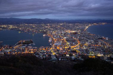 Hakodate, Japonya - 30 Kasım 2019: Hakodate Dağı 'ndan Milyon Dolarlık Manzara, etekten zirveye giden yolu takip edin. Parıldayan şehir ışıklarının ve okyanusun zifiri karanlığının karşıtlığı tarif edilemez derecede güzeldir..