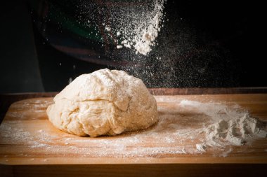 Hamur tahtanın üzerinde, koyu bir arka planda bir un serpintisi.