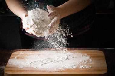 Aşçının elleri hamuru tutuyor, pizza yapıyor. Un koyu arkaplanda uçar.