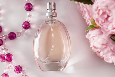 Beyaz arka planda parfüm şişesi ve çiçekler. Boncuk ve çiçeklerin arka planında mis kokulu bir parfüm. Hafif arka planda bakım için aksesuarlar.