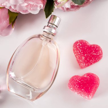 Hafif arka planda bir şişe parfüm, çiçekler ve kalpler. Hafif arka planda kalp şeklinde zarif parfümler ve tatlılar. Kare fotoğraf, Sevgililer Günü hediyesi konsepti..