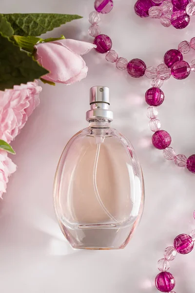 Perfume bottle and flowers on a white background. Delicate fragrant perfumes in an elegant bottle on the background of flowers and accessories. Pastel colors, vertical photo.