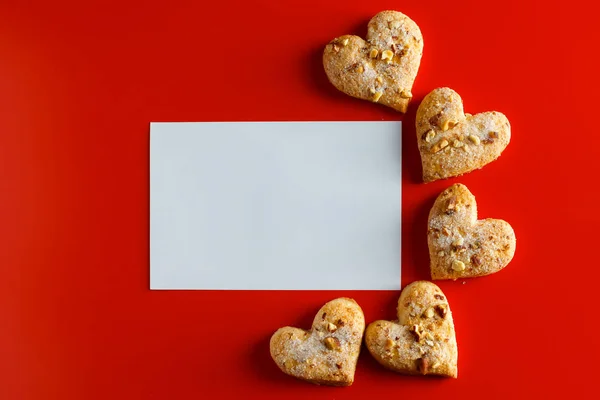 Cookies on a red background and a blank greeting card. Empty greeting card and heart-shaped cookies on a red background. Place for text