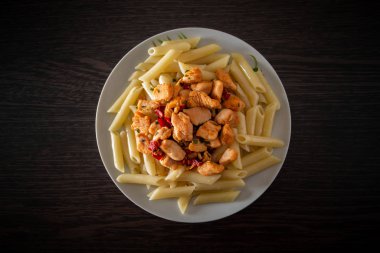 Domates soslu tavuk ve sebzeli makarna. Bir tabak makarna ve kızarmış tavuk. Arka planda, üst tarafta.