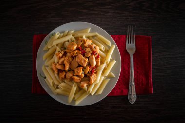 Domates soslu tavuk ve sebzeli makarna. Bir tabak makarna ve domates soslu tavuk çatalın yanındaki masada.