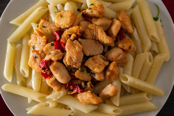 Penne pasta with chicken and vegetables in tomato sauce. Penne pasta with fried chicken and vegetables closeup