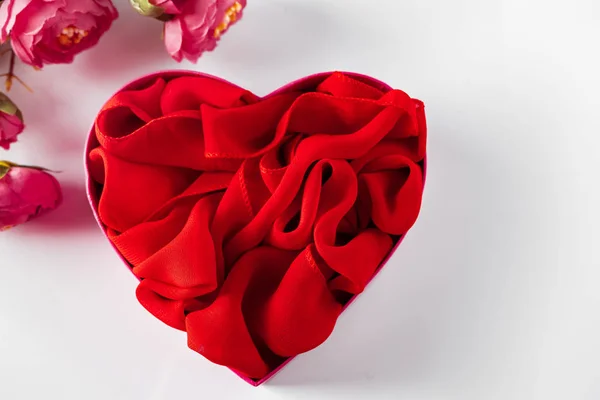 Red heart shaped gift box and flowers on white background. Holiday gift, heart shaped box with silk ribbon and flowers on a white background.
