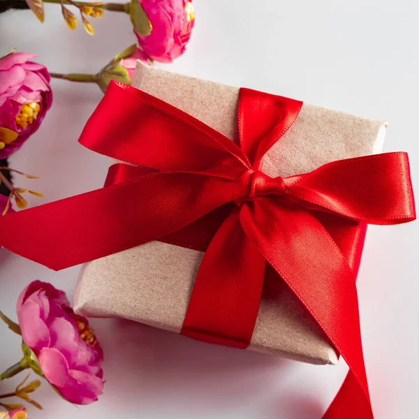 Gift box with red ribbon and flowers on a white background. Gift box with red ribbon and delicate pink flowers on a white background. Surprise on Women\'s Day and Mother\'s Day.