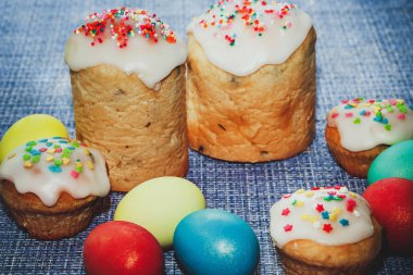 Kutlama kompozisyonu - Tatlı kremalı Paskalya pastaları ve mavi arka planda boyanmış yumurtalar.