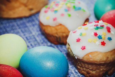 Kutlama kompozisyonu - Tatlı kremalı Paskalya pastaları ve mavi arka planda boyanmış yumurtalar.