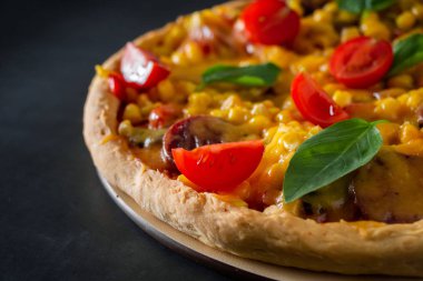 Domatesli ve fesleğenli pizza. Siyah arka planda domatesli, peynirli ve fesleğenli İtalyan pizzası. Siyah arka planda mısır ve peynirli pizza dilimi. Dikey fotoğraf, metin için yer.
