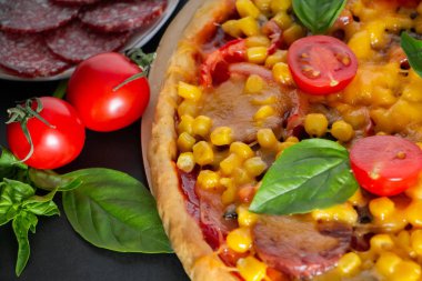 Domatesli ve fesleğenli pizza. Siyah arka planda domatesli, peynirli ve fesleğenli İtalyan pizzası. Siyah arka planda mısır ve peynirli pizza dilimi. Dikey fotoğraf, metin için yer.