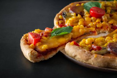 Kiraz domatesli lezzetli pizza ve siyah arka planda dilimlenmiş dilim. Yuvarlak bir tahtada peynirli ve kiraz domatesli leziz İtalyan pizzası, dilimlenmiş üçgen bir parça. Akdeniz mutfağının özgün ulusal yemeği.