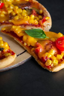 Gri arka planda pizza. Akdeniz mutfağının özgün ulusal yemeği. Yuvarlak bir tahtada peynirli ve kiraz domatesli taze pizza, dilimlenmiş. Dikey fotoğraf