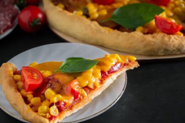 Siyah arka planda kirazlı ve fesleğenli pizza dilimi. Ulusal İtalyan yemeklerini hazırlamak için gerekli malzemeler. Çeri domatesli taze pizza ve siyah arka planda yeşil fesleğen. Dikey fotoğraf, metin için yer.