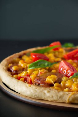 Domatesli ve fesleğenli pizza. Siyah arka planda domatesli, peynirli ve fesleğenli İtalyan pizzası. Siyah arka planda mısır ve peynirli pizza dilimi. Dikey fotoğraf, metin için yer.