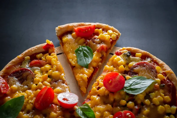 Tasty pizza with cherry tomatoes and sliced slice on a black background. Delicious italian pizza with cheese and cherry tomatoes on a round board, sliced triangular piece. Authentic national dish of Mediterranean cuisine.