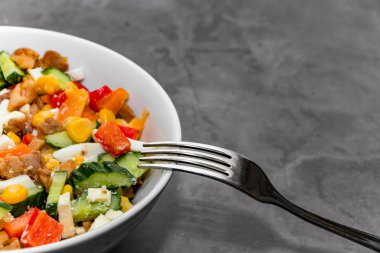 Parlak sebze salatası ve gri beton arka planda tavuk. Sağlıklı bir diyet için lezzetli bir salata yapıyorum. Tabakta sebze salatası ve gri arka planda çatal. Metin için yer