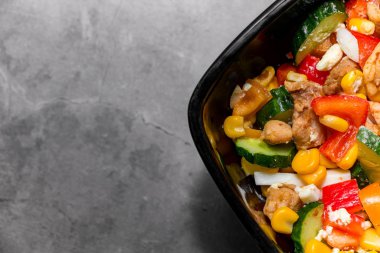 Parlak sebze salatası ve gri beton arka planda tavuk. Sağlıklı bir diyet için lezzetli bir salata yapıyorum. Beton bir arka planda parlak bir salata ile siyah bir plakanın yakın plan fotoğrafı.