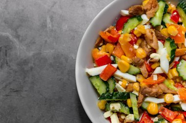 Parlak sebze salatası ve gri beton arka planda tavuk. Sağlıklı bir diyet için lezzetli bir salata yapıyorum. Sağında gri beton arka planda sebze salatası olan bir tabağın parçası. Yatay bileşim, metin için yer.