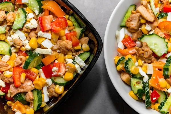 Bright vegetable salad with chicken on a gray concrete background. Making a delicious salad for a healthy diet. Two bowls of vegetable salad with chicken close-up