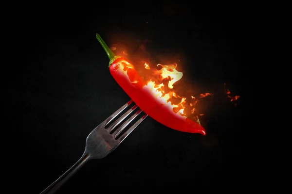 黒を基調としたフォークに赤唐辛子を焼く 炎の中のフォークに赤唐辛子 辛い食べ物のシンボル — ストック写真
