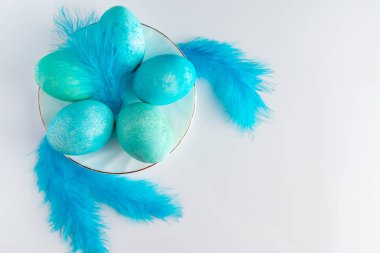 Açık arkaplanda mavi paskalya yumurtası ve tüylerinin bileşimi. Beyaz arka planda mavi paskalya yumurtası ve kuş tüyü boyanmış. Metnin için yer.