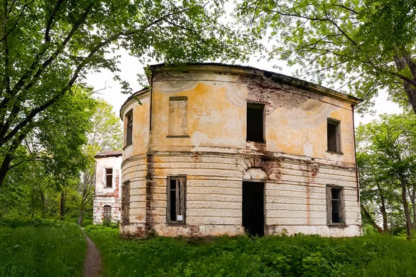 Old abandoned manor house with boarded up windows. The building of an old abandoned manor among green trees