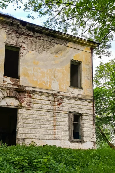 Old abandoned manor house with boarded up windows. Ruined building of an old manor with broken windows among green trees