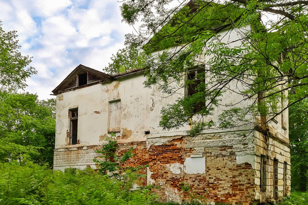 Old abandoned manor house with boarded up windows. The building of an old abandoned manor among green trees