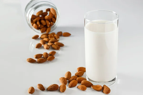 A glass of almond milk on a white background. Lactose-free vegetable diet milk. Gluten free almond drink on a blue background. Super Food - A glass of almond milk for a healthy diet. Trending food, vertical photo. Place for your text.