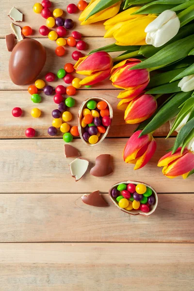 Bright multi-colored tulips and chocolate Easter eggs on a wooden background. Festive design, place for text, vertical photo
