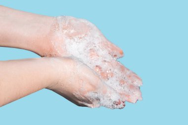 Bir kadın ellerini mavi arka planda sabunla yıkıyor ve dezenfekte ediyor. Coronavirus koruması. Kişisel sağlık ve sağlık hizmetleri.