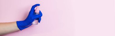 Mavi lateks eldivenli bir el dezenfektan tutar. Koronavirüse karşı önleyici koruma kavramı. Temizlik için antiseptik kullanımı.