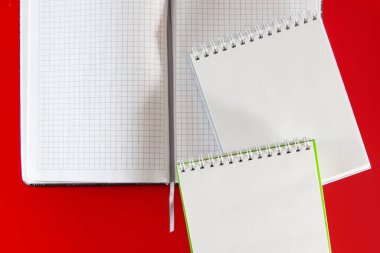 Tasarım için minimalist bir düzen. Ofis malzemeleri - kırmızı arka planda defterler ve kalemler. Kırmızı arkaplandaki notlarınız için boş bir defter açın