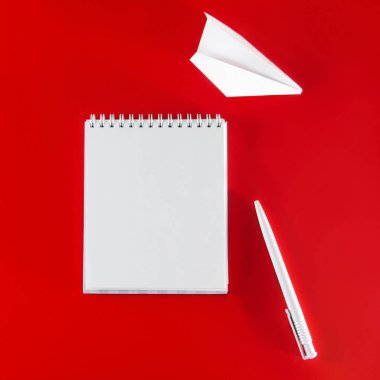 Kırmızı arka planda ofis malzemeleri. Boş defter, kalem ve gözlük. Tasarım için minimalizm tarzında bir düzen.
