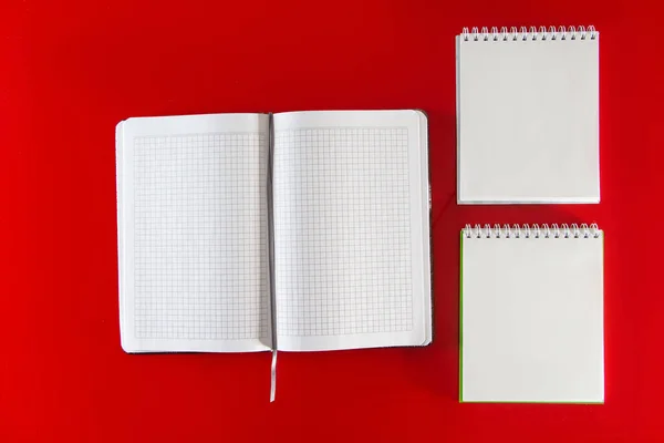 Minimalistic layout for design. Office supplies - notebooks and pens on a red background. Open blank notebook for your notes on a red background