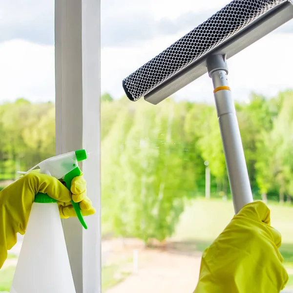 Window washing and home cleaning. Housekeeper in yellow gloves washes and wipes dirty glass.