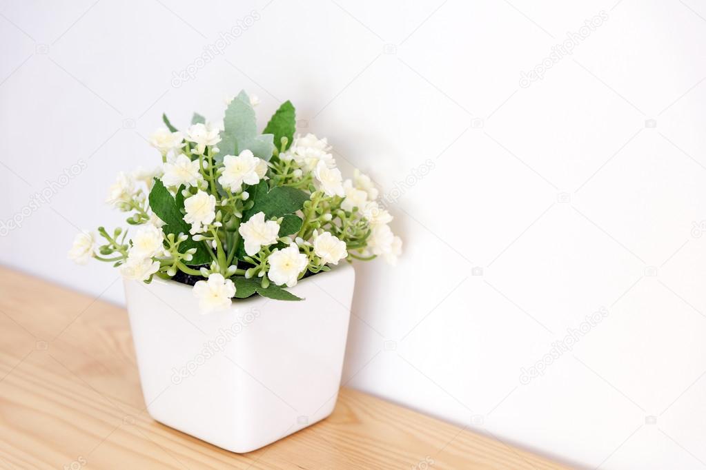 The artificial jasmine flower in the pot at the wooden table wit