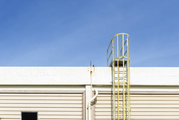 The yellow fire escape stair attach at the factory building with the blue sky