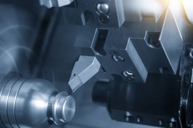 Metal işlemde kullanılan CNC torna makinesi açık mavi sahnede metal şaft parçalarını kesiyor. CNC dönüşüm makinesinin yüksek teknolojili metal işlemesi .