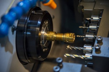 Çoklu görev yapan CNC torna makinesi İsviçre usulü pirinç şafta tıkırdıyor. CNC programı tarafından kontrol edilen yüksek teknolojili metal çalışma süreci