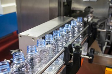 Su fabrikasındaki işlemleri tamamlamak için taşıma bandındaki korkuluktaki evcil hayvan şişeleri. Fabrikadaki otomatik doldurma makinesinin içme suyu üretim süreci.. 