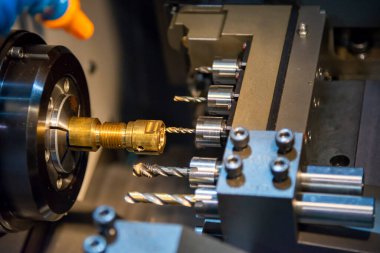 Çoklu görev yapan CNC torna makinesi İsviçre usulü pirinç şafta tıkırdıyor. CNC programı tarafından kontrol edilen yüksek teknolojili metal çalışma süreci