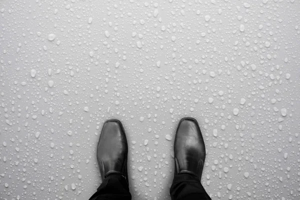 Businessman in black shoes standing on white wet floor. Water drop on the floor. Caution, slippery floor.