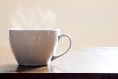 Ahşap masa ve sabah ışık beyaz fincan sıcak kahve parlıyor.