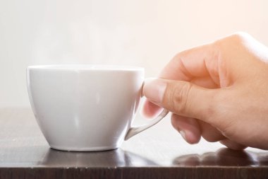 Ahşap masa ve sabah ışık beyaz fincan sıcak kahve parlıyor.