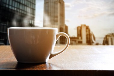 Kahve dükkanı veya kafe ahşap masa üzerinde beyaz fincan sıcak kahve. Sabah yüksek kule üstünde belgili tanımlık pencere. Pencerenin dışındaki Şehir Manzaralı.