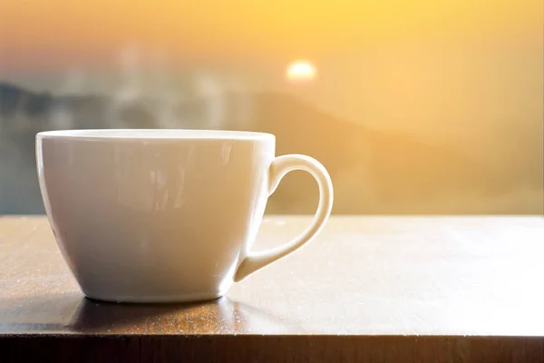Hot coffee in white cup on wooden table in the morning when sunrise from the mountain. Relax and rest time.