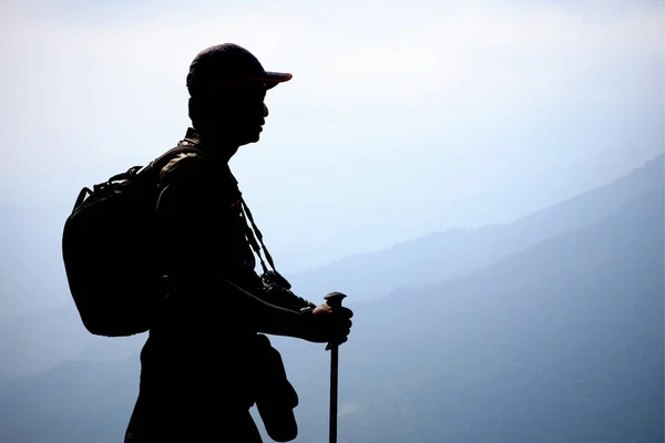 Silhouette trekker with backpack, trekking pole and camera